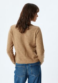 Pull en laine couleur camel avec un col rond et des poignets côtelés, associé à un jean en denim bleu. Texture douce, ajusté à la taille.