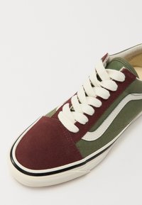 Lågskor i sneakers-stil med en vinröd mocka tådel, olivfärgad canvasovandel, krämfärgade snören och vit sidremsa. Gummisulor med svarta accenter.