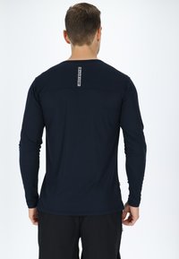 Langärmliges navyblaues Hemd mit rundem Ausschnitt. Verfügt über ein vertikales Logoschild im oberen Rückenbereich und ein nahtloses Schulterdesign. Glatte Stofftextur.