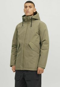 Veste à capuche vert olive avec fermeture éclair sur le devant, poches latérales et cordons de serrage ajustables. Présente une texture lisse et mate avec une coupe droite.