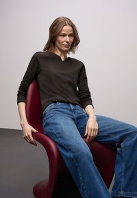 Ciemny prążkowany top z długim rękawem oraz szerokie niebieskie dżinsy noszone przez osobę siedzącą na czerwonym ergonomicznym krześle na jasnym tle.