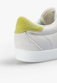 Białe skórzane sneakersy z szarymi zamszowymi akcentami i zielonym zamszowym obcasem. Posiadają teksturowaną białą gumową podeszwę oraz wytłaczane detale na pięcie.
