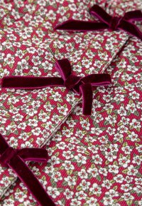 Tela floral con flores blancas y acentos rojos sobre un fondo burdeos, complementada con pequeños lazos de terciopelo en color a juego.
