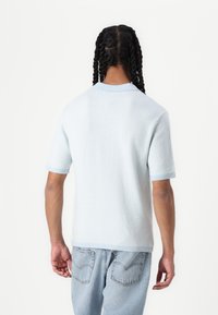 Ανοιχτό μπλε κοντομάνικο πουλόβερ με υφαντό σχέδιο, ριγέ γιακά και μανίκια, και χαλαρή εφαρμογή, σε συνδυασμό με μπλε τζιν παντελόνι.