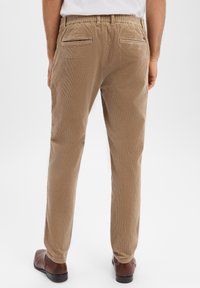 Spodnie sztruksowe w jasnobrązowym kolorze z prążkowaną teksturą, wyposażone w elastyczną talię i dwie tylne kieszenie. Jednolity kolor bez wzorów.