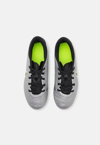 Chaussures de soccer grises avec une surface texturée, des lacets noirs et une semelle intérieure verte néon. Présente un logo noir et jaune sur le côté.