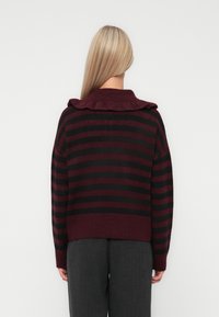 Burgundy ja musti triibuline lühike kampsun, millel on soonikuga volangkaelus. Pehme kudumistekstuuri ja pikkade varrukatega ning langetatud õlavarre disain.