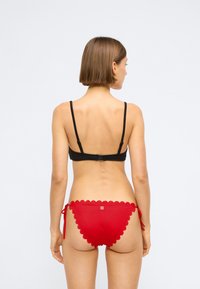 Must mustriga mustriga bralette, mille säädettavad rihmad, mis on ühendatud punaste laineliste bikiinide pükstega, millel on külgedel sidemed ja logo seljal.