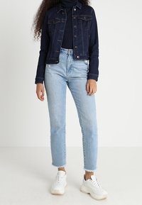 Džínsová bunda tmavě modré barvy, doplněná přiléhavým černým rolákem. Světle modré džíny lehce zkrácené s ohrnutými lemy. Bílé tenisky dokončují vzhled.