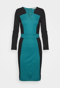 Robe près du corps longueur genou en bleu sarcelle et noir, manches longues, col en V, avec un design en blocs de couleur créant un effet taille cintrée.