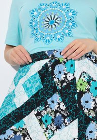 Un top azzurro chiaro con un design grafico circolare, abbinato a una gonna floreale multicolore con un motivo a patchwork in blu, nero e verde.