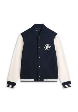 Marineblå og hvit collegejakke med knapper foran, stripete ribbestrikkede mansjetter og fald, og hvit brodert "TH"-logo på brystet.