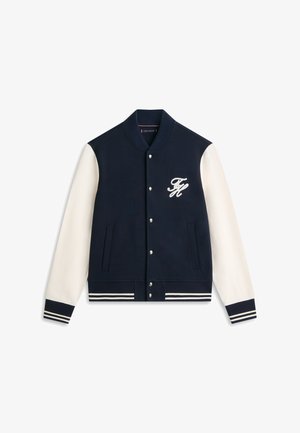Marineblå og hvit collegejakke med knapper foran, stripete ribbestrikkede mansjetter og fald, og hvit brodert "TH"-logo på brystet.