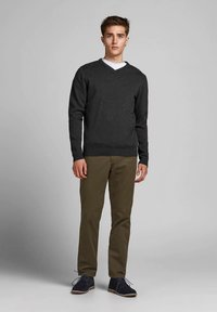 Jemno ogleno sivi pulover z v-izrezom, kombiniran z olivno zelenimi hlačami, z rebrastim robom in manšetami, nošen z mornarsko modrimi semiš čevlji.