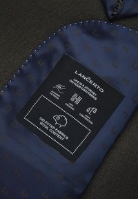 Metka Lancerto zawiera granatowy satynowy materiał z wzorem. Tekst wskazuje instrukcje dotyczące pielęgnacji tkaniny oraz zawartość wełny. Zauważono lekką konstrukcję.