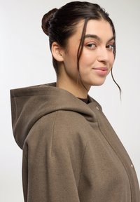 Cappotto marrone con cappuccio realizzato in tessuto morbido, caratterizzato da una vestibilità comoda, chiusura con bottoni a scatto e una superficie liscia. Design semplice senza motivi visibili.