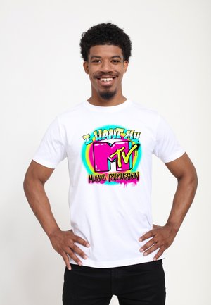 T-shirt bianco in cotone con una grafica colorata che presenta il testo "Voglio il mio MTV" e "TELEVISIONE MUSICALE" in un vivace rosa, blu e giallo.