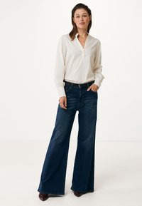 Crème-kleurige blouse met een V-hals en gedrapeerde mouwen, gecombineerd met donkerblauwe hoge taille wijde jeans en een zwarte riem.