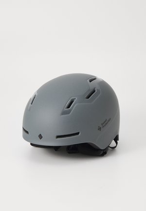 Grå hjelm med ventilasjonsspor, lettvektig design, matt finish og justerbare stropper. Merkevaren logo synlig på siden.