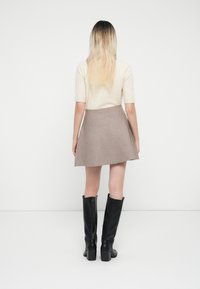 Lys beige kortermet topp i kombinasjon med en taupe A-linjet skirt, iført knelange svarte høye støvler. Glatt tekstur, enkelt design.