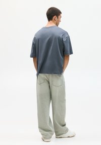 Tričko s krátkým rukávem uvolněného střihu v modré barvě, které je kombinováno s volnými světle zelenými kalhotami, jež mají zadní kapsy a ležérní design.
