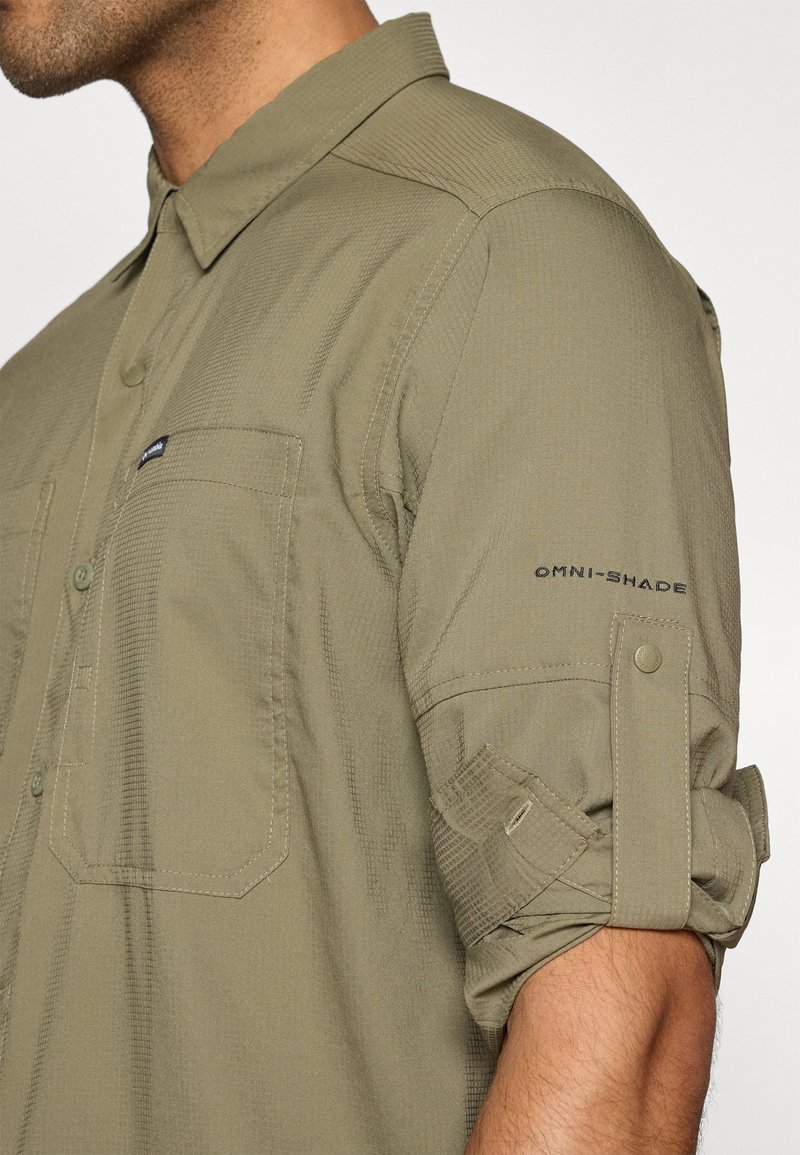 Helles olivgrünes Hemd aus strukturiertem Stoff. Verfügt über eine durchgehende Knopfleiste, zwei Brusttaschen und hochgekrempelte Ärmel mit OMNI-SHADE-Branding.