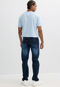 Camiseta de manga corta azul claro combinada con jeans de mezclilla azul oscuro, que presentan un corte recto clásico y detalles en los bolsillos traseros. Zapatillas blancas.