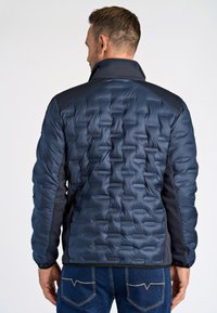 Mörkblått puffjacka med en texturerad, kviltad design, som har en hög krage och kontrasterande mörka nät- och tygdetaljer.