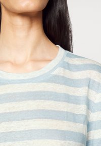 Kevyt, struktuurilla varustettu neulepaita, jossa on vaaleansinisiä ja luonnonvalkoisia vaakaraitoja. Pyöreä kaula-auko ja rento malli.