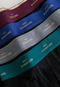 Négy pár rugalmas derékpántú alsónemű különböző színekben: bordó, kék, szürke és türkiz, mindegyiken arany betűkkel "NEXT SIGNATURE" felirat található.