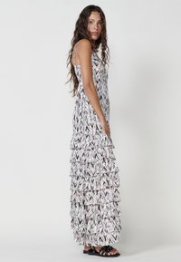 Robe maxi dans un motif abstrait noir, blanc et rose pâle avec des couches froncées, des bretelles réglables et une silhouette fluide.