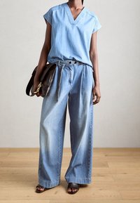 Lyseblå denim-top med korteærmer og V-udskæring, parret med vide, lyseblå denimbukser. Sort håndtaske og åbne sorte sandaler.