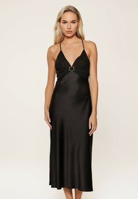Robe midi en satin noir avec un décolleté en V profond, des fines bretelles et un détail en anneau métallique central à la taille. Texture lisse, coupe ajustée.