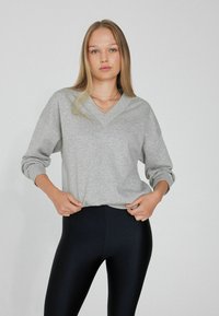 Sudadera gris de cuello en V con mangas largas, hecha de un tejido suave; combinada con leggings negros de cintura alta. Diseño simple y casual.