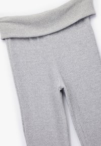 Jasnoszare legginsy z prążkowanym, złożonym pasem. Materiał jest miękki i teksturowany, z gładkim wykończeniem. Brak widocznych wzorów lub akcentów.