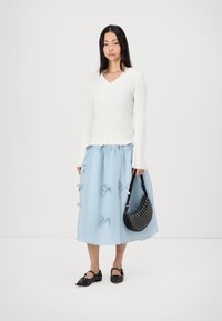 White ribbed long-sleeve top, light blue skirt with bow accents, black embellished handbag, and black pointy-toed flats.
