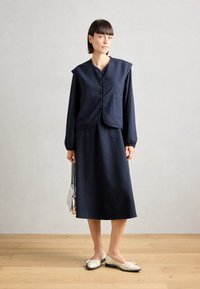 Marineblauw pinstripe outfit met een colbert met knopen en een bijpassende rok. Gekenmerkt door beige schoenen met zwarte teentjes. Zilveren tas.