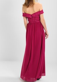 Lång off-shoulder klänning i fuchsia med spetstopp, flödande kjol och knappdetalj bak. Slätt, lätt tyg.