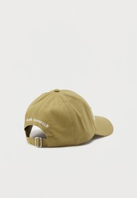 Kaki kokvilnas cepure ar izliekta mali, regulējama josta un izšūts "KARL LAGERFELD" logo aizmugurē. Gluda tekstūra, ikdienišķs dizains.