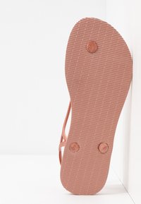 Chinelo rosa com uma sola de borracha texturizada, apresentando dois acentos circulares na parte inferior e tiras finas na parte superior para um ajuste seguro.