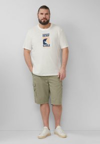 Lichtbeige t-shirt met een grafische print in blauw en perzik; olijfgroene cargoshorts met zijzakken; witte sneakers.