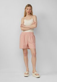 Gestreepte roze shorts met een elastische tailleband, gemaakt van lichtgewicht stof. Gecombineerd met een crème tanktop en beige plateau sandalen.