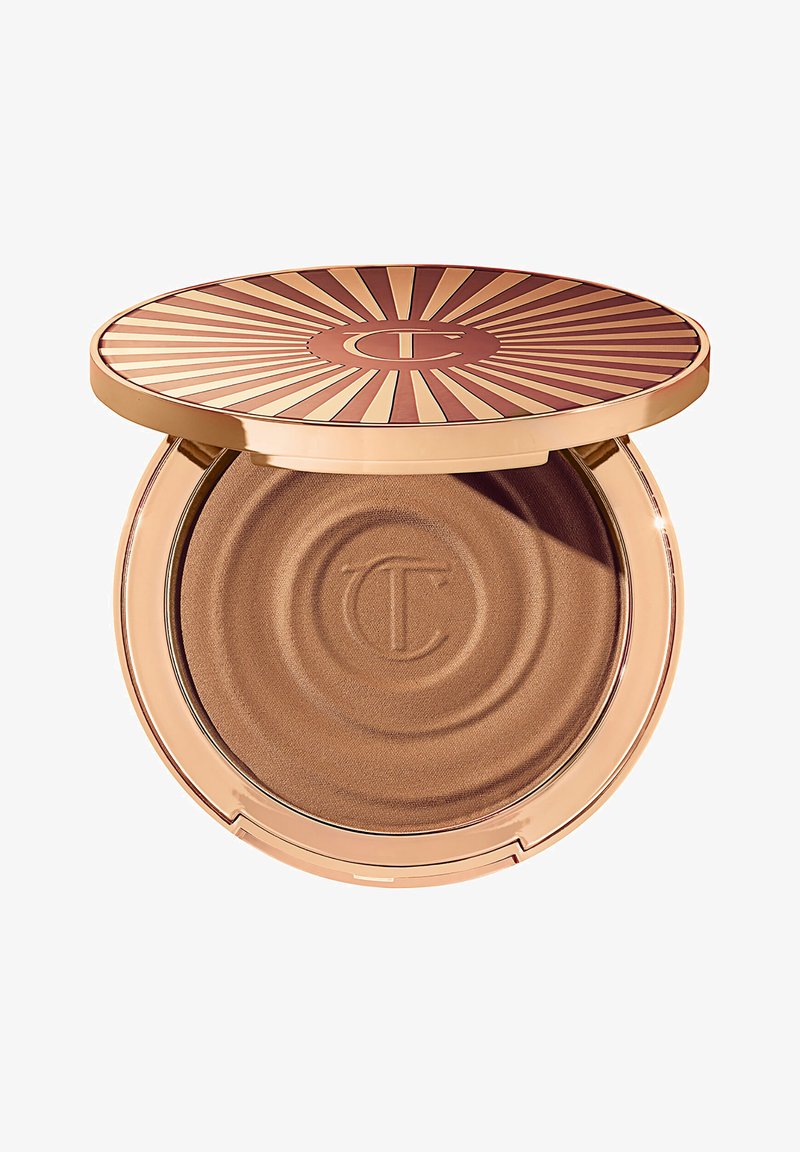 Bronzer en poudre dans un compact rond avec un couvercle au design en rayons de soleil. Le produit a une texture bronze métallique lisse avec un imprimé circulaire.
