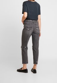 Svarta, högmidjade jeans med slitna detaljer och en avsmalnande passform, kombinerat med en mörk t-shirt och svarta loafer-skor.