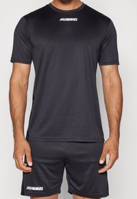 Czarny sportowy T-shirt z krótkim rękawem, gładka faktura, z białym logo "HUMMEL" na piersi, w komplecie z dopasowanymi szortami.