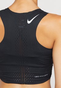 Černý atletický crop top s prodyšným designem, který obsahuje perforovaný vzor, kulatý výstřih a bílý logo Nike na zádech.