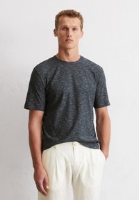 Graues T-Shirt mit kurzen Ärmeln und strukturiertem, melierten Muster. Rundhalsausschnitt, lässiger Schnitt, kombiniert mit hellen Hosen.