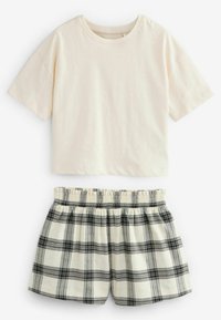 Jasnobeżowy bawełniany T-shirt z krótkim rękawem, w połączeniu z szortami w czarno-białą kratę, posiadającymi elastyczny pas i marszczoną strukturę.