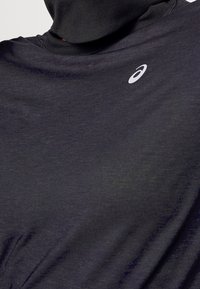 Maglietta sportiva nera con collo alto e maniche lunghe. Tessuto leggero con un piccolo logo bianco sul petto. Texture liscia.