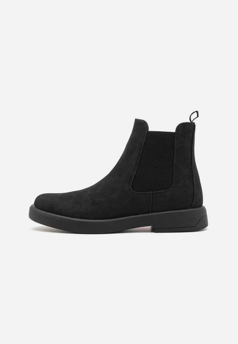 Botas Chelsea negras de ante con paneles laterales elásticos y una lengüeta. Presentan un acabado texturizado y una suela plana de goma duradera.